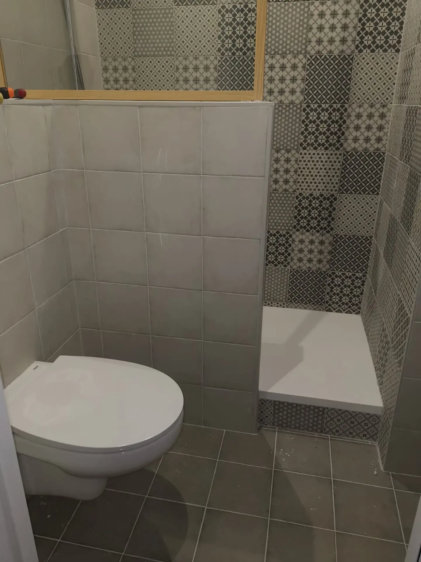 Salle de bains avec WC suspendu et douche habillée de carreaux ciment à motifs gris et blancs